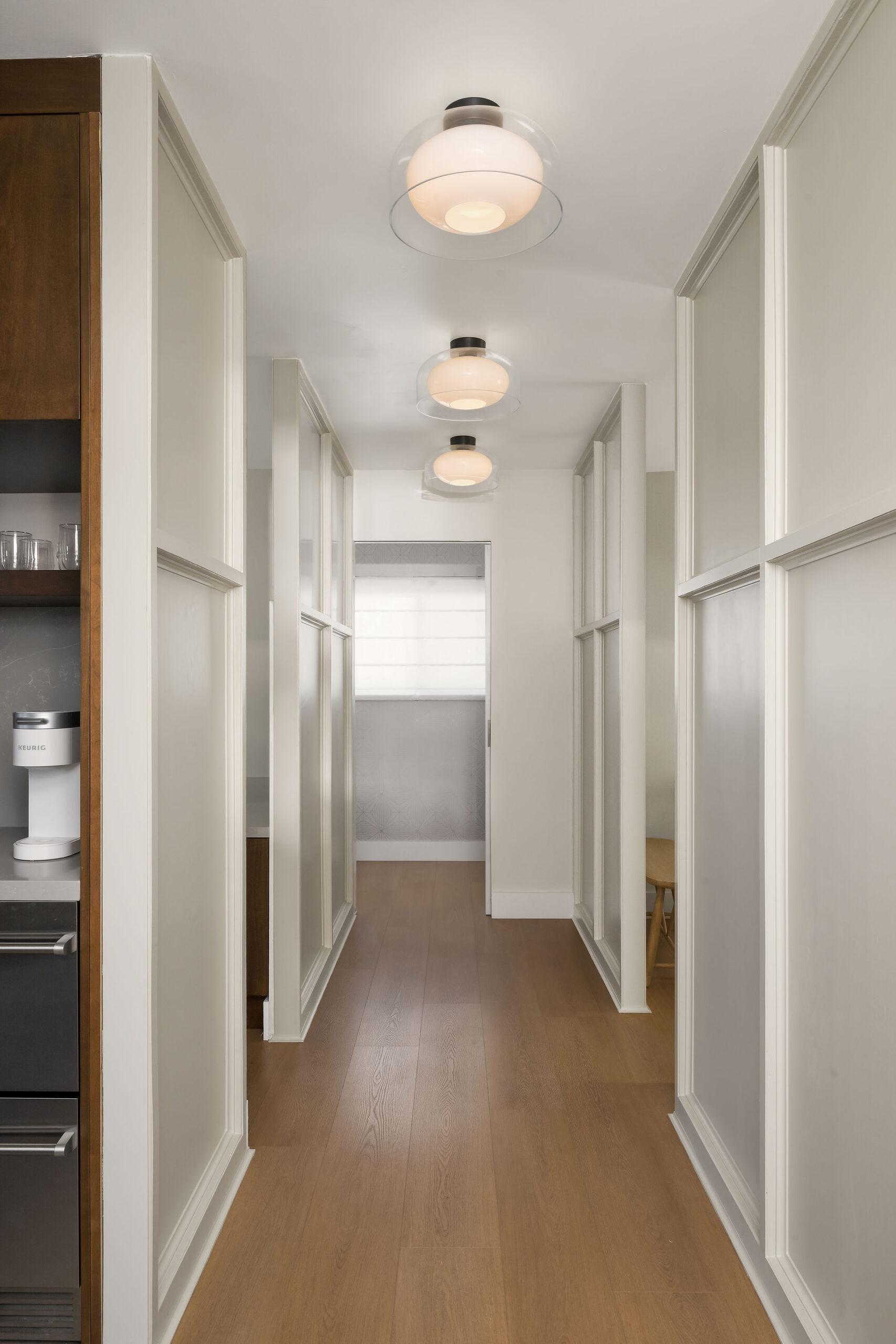 Spa-inspired dental office hallway with engineered wood flooring, frosted glass sliding doors, and globe ceiling lights