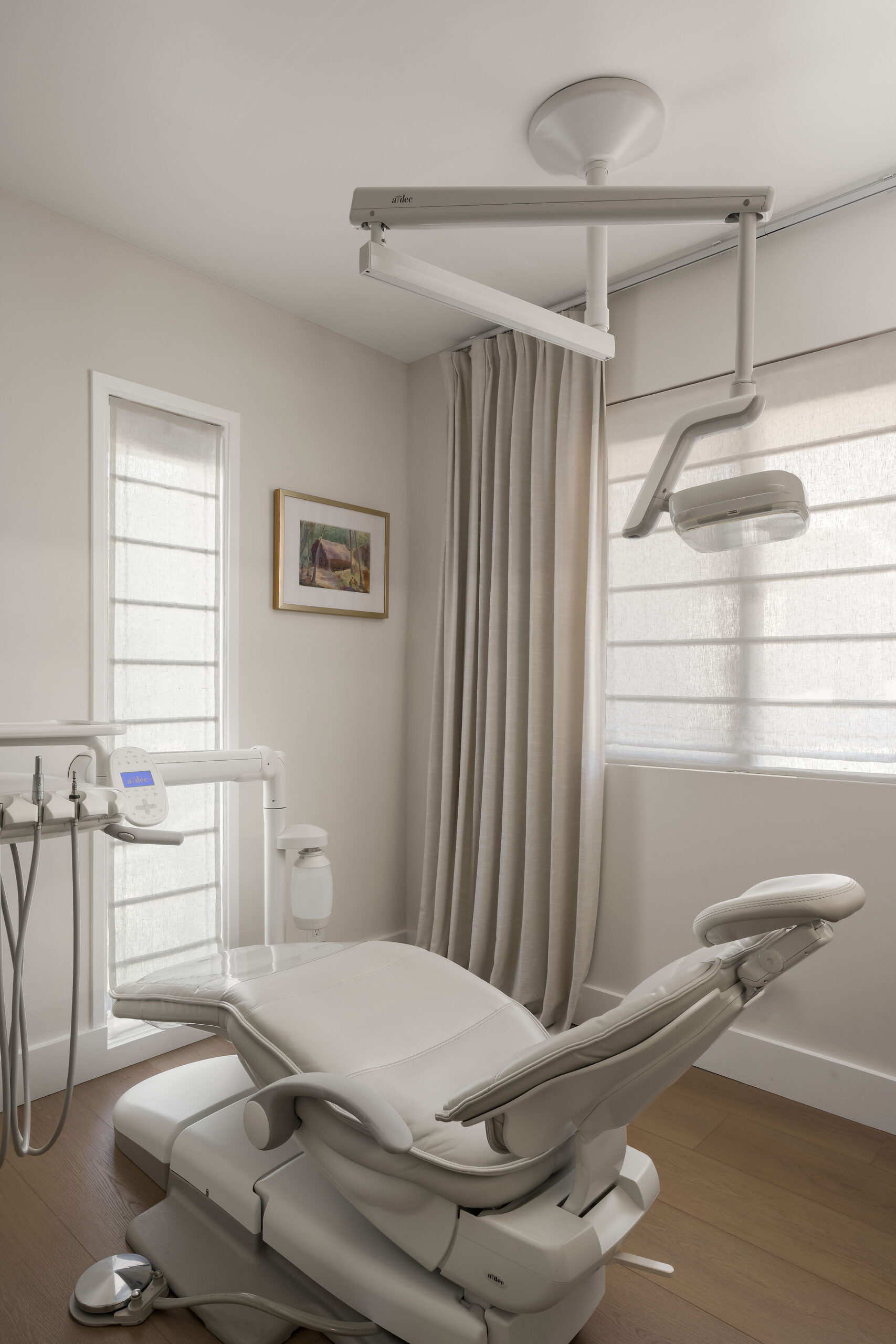 Calm dental treatment room with neutral drapery, white Roman shades, and modern dental chair